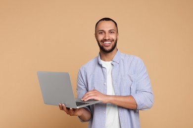 Photo of Smiling young man working with laptop on beige background. Space for text