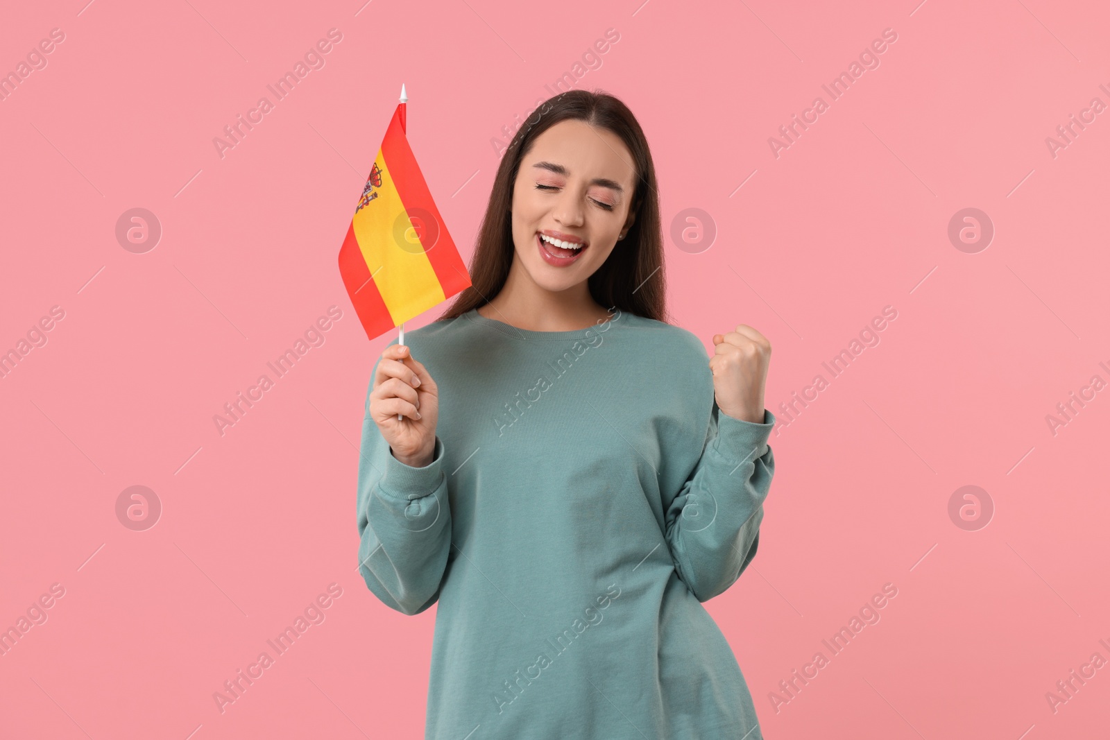 Photo of Emotional young woman holding flag of Spain on pink background