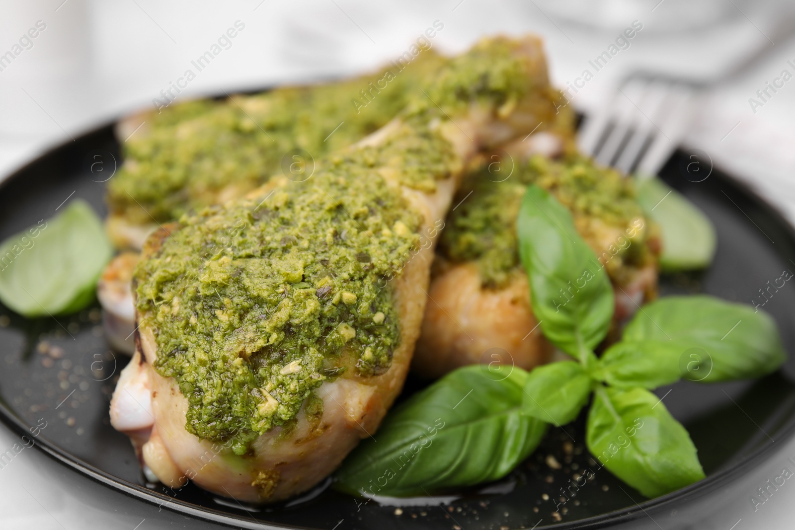 Photo of Delicious fried chicken drumsticks with pesto sauce and basil on white table, closeup