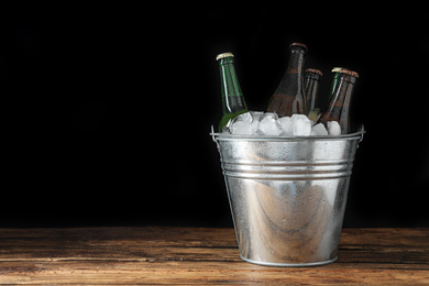 Photo of Metal bucket with bottles of beer and ice cubes on wooden table. Space for text