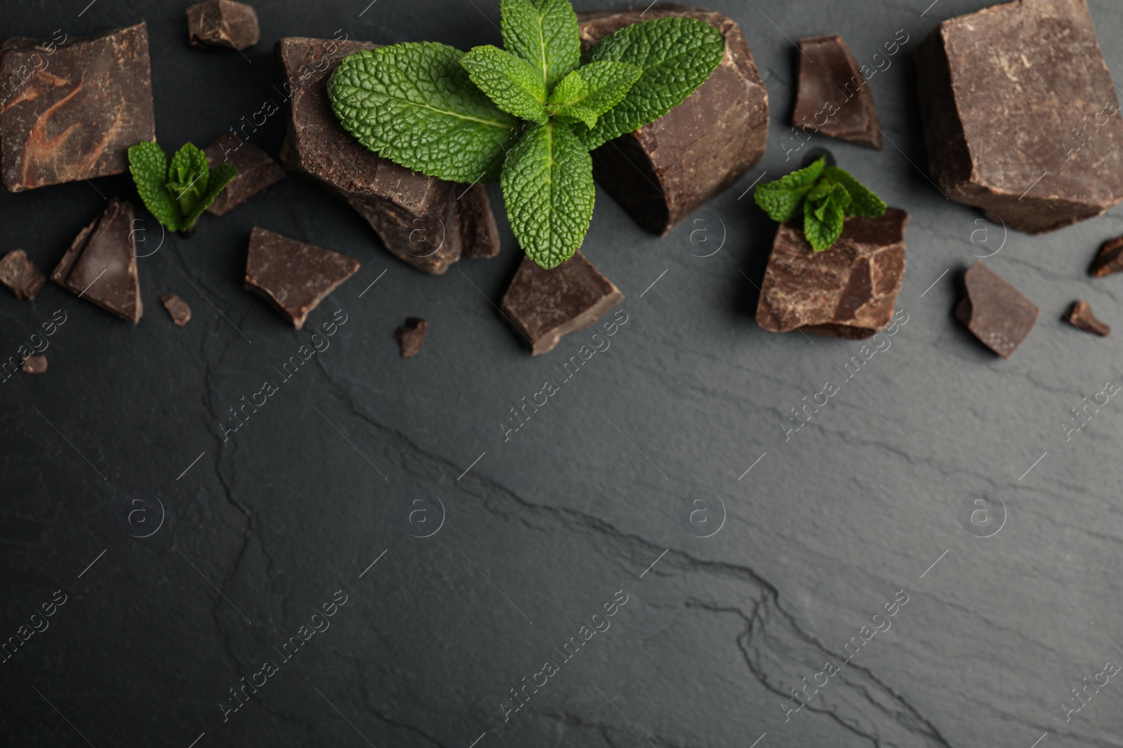 Photo of Tasty dark chocolate pieces with mint on black table, flat lay. Space for text