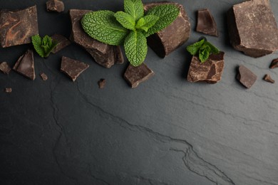 Tasty dark chocolate pieces with mint on black table, flat lay. Space for text