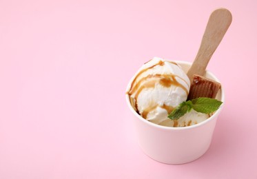 Tasty ice cream with caramel sauce, mint and candy on pink table, space for text