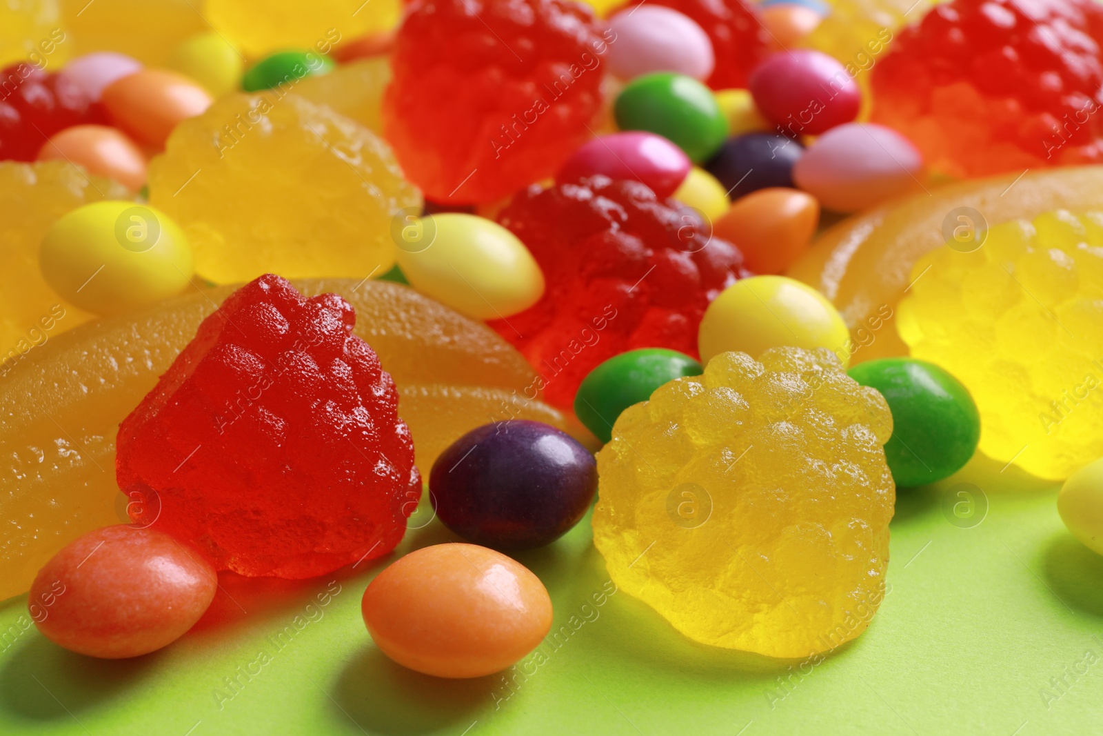 Photo of Delicious dragee and gummy candies on green background, closeup