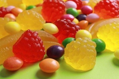 Delicious dragee and gummy candies on green background, closeup