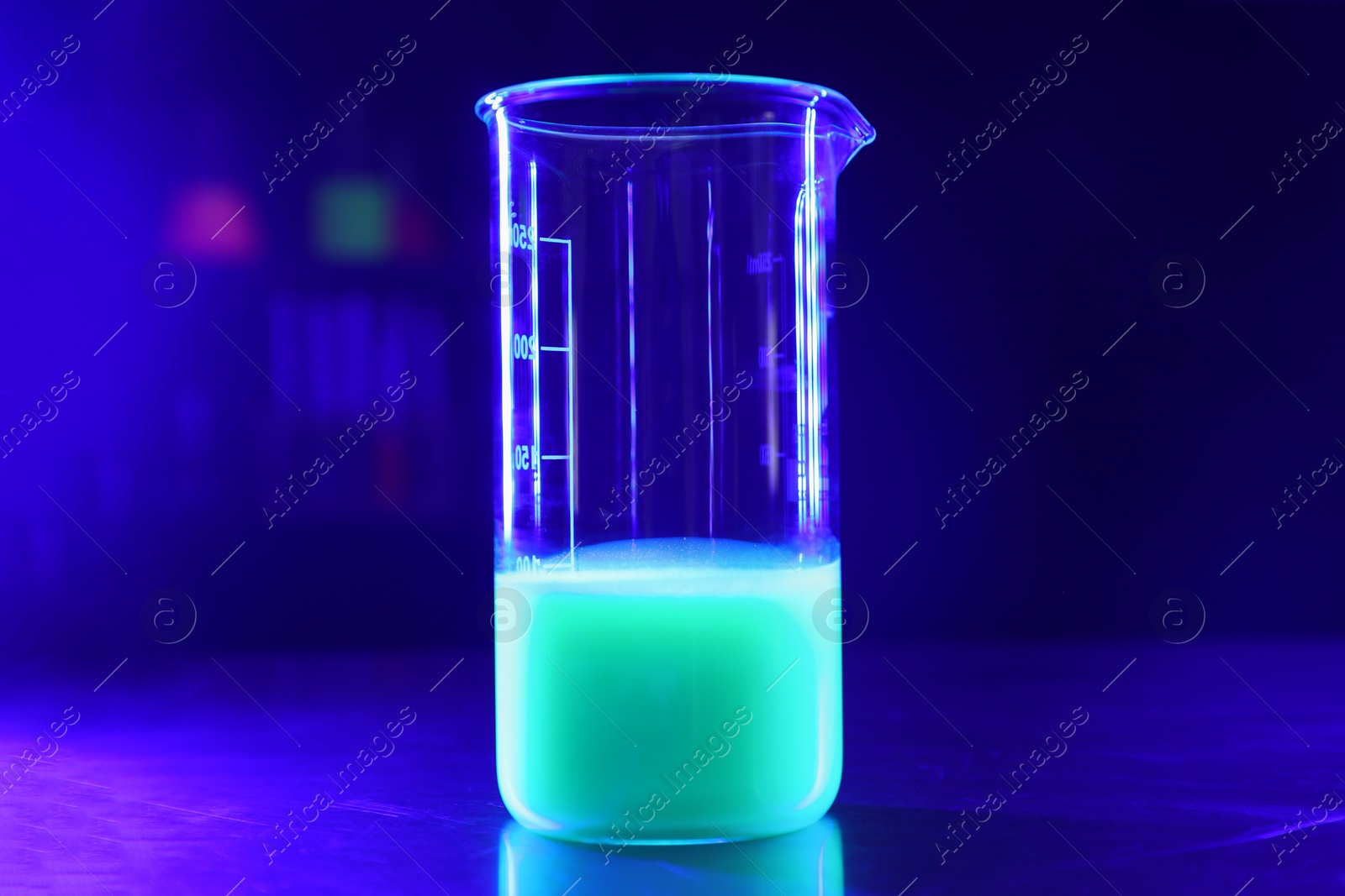 Photo of Laboratory beaker with luminous liquid on table against dark blue background, space for text