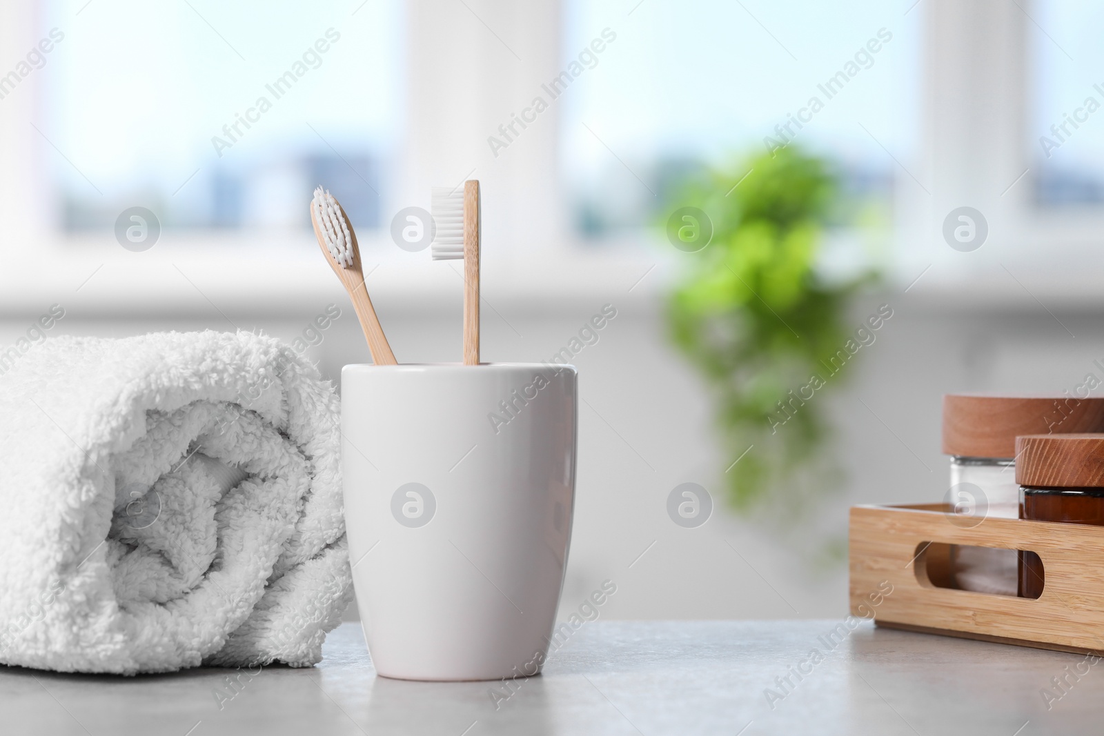 Photo of Bamboo toothbrushes in holder, towel and cosmetic products on light grey table indoors. Space for text