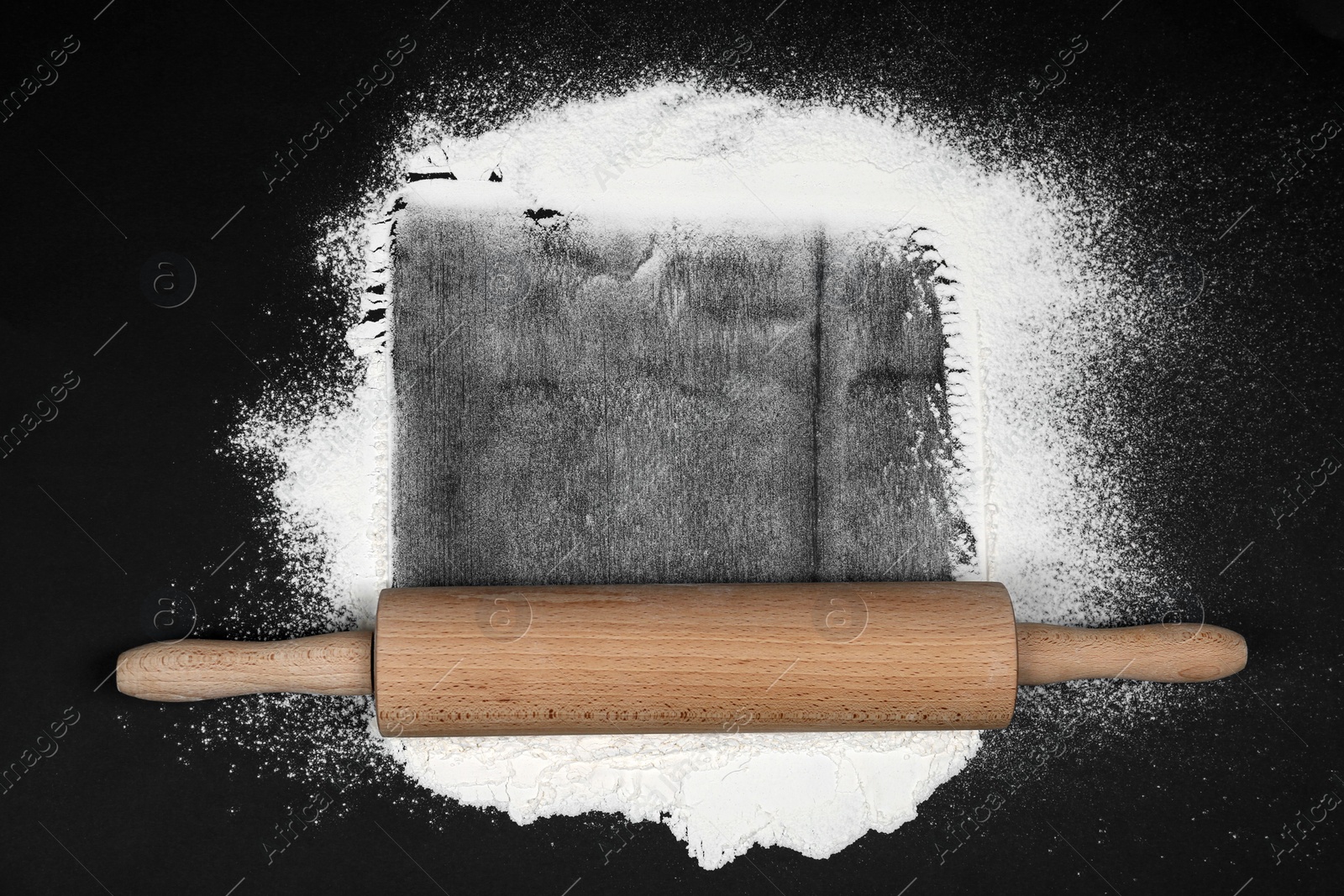 Photo of Flour and rolling pin on black table, flat lay