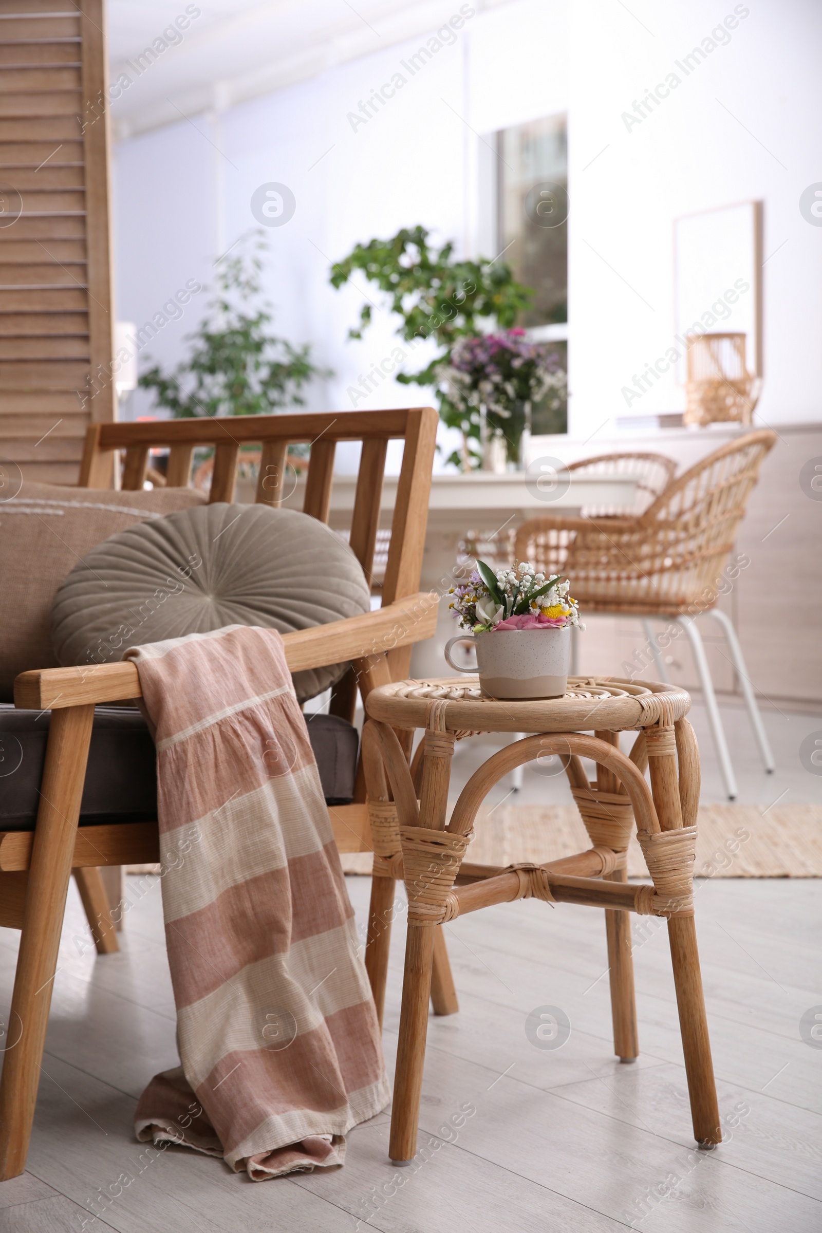 Photo of Stylish wooden stool with bouquet of flowers near armchair in room. Interior element