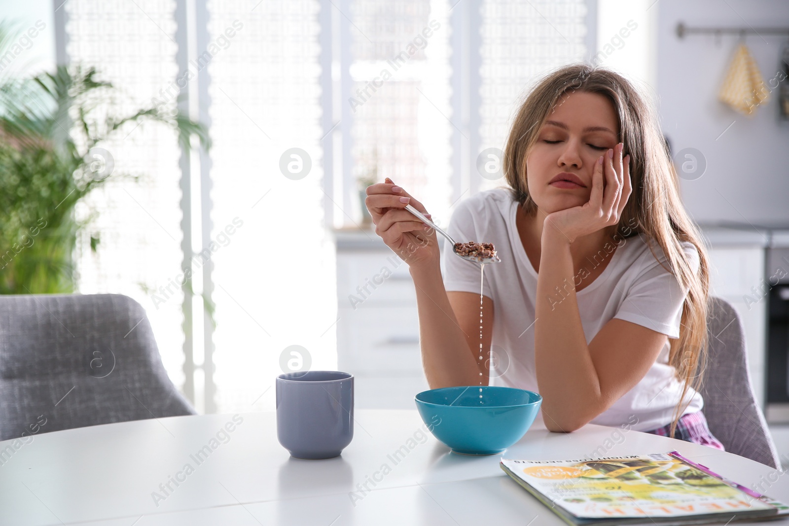 Photo of Sleepy young woman eating breakfast at home in morning