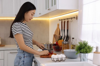 Photo of Cooking process. Beautiful woman cutting tomato in kitchen