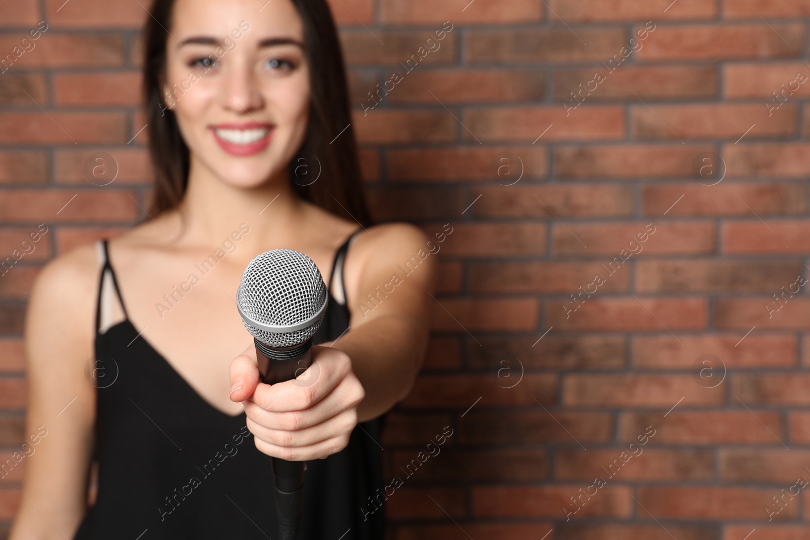 Photo of Young woman holding microphone near brick wall. Space for text