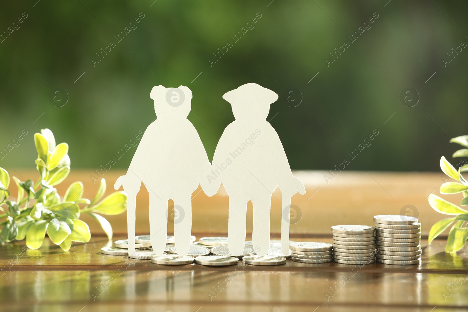 Photo of Pension savings. Figure of senior couple, coins and green twigs on wooden table outdoors