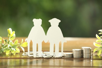 Photo of Pension savings. Figure of senior couple, coins and green twigs on wooden table outdoors