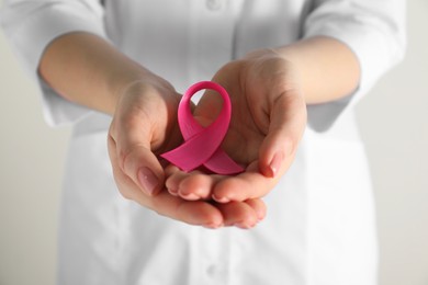 Photo of Mammologist with pink ribbon on light background, closeup. Breast cancer awareness