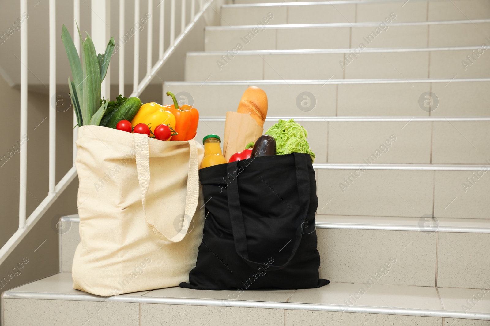 Photo of Tote bags with vegetables and other products on stairs indoors. Space for text