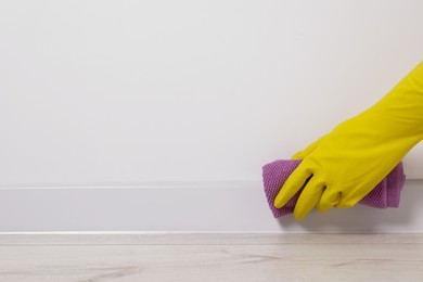 Photo of Woman in protective glove cleaning plinth with washcloth indoors, closeup. Space for text