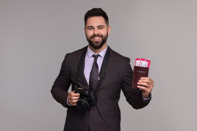 Happy businessman with passport, tickets and camera on grey background