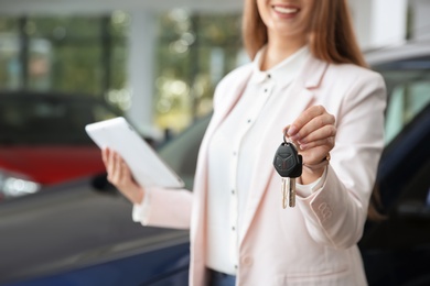 Photo of Woman with tablet and car keys in modern auto dealership, closeup