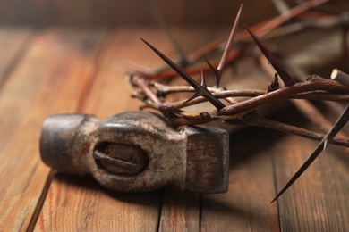 Crown of thorns and hammer on wooden table, closeup. Easter attributes
