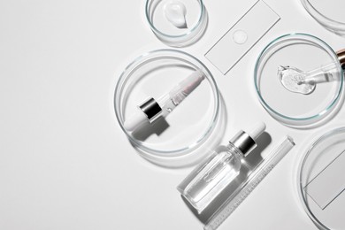 Photo of Flat lay composition with petri dishes and samples of cosmetic serums on white background. Space for text