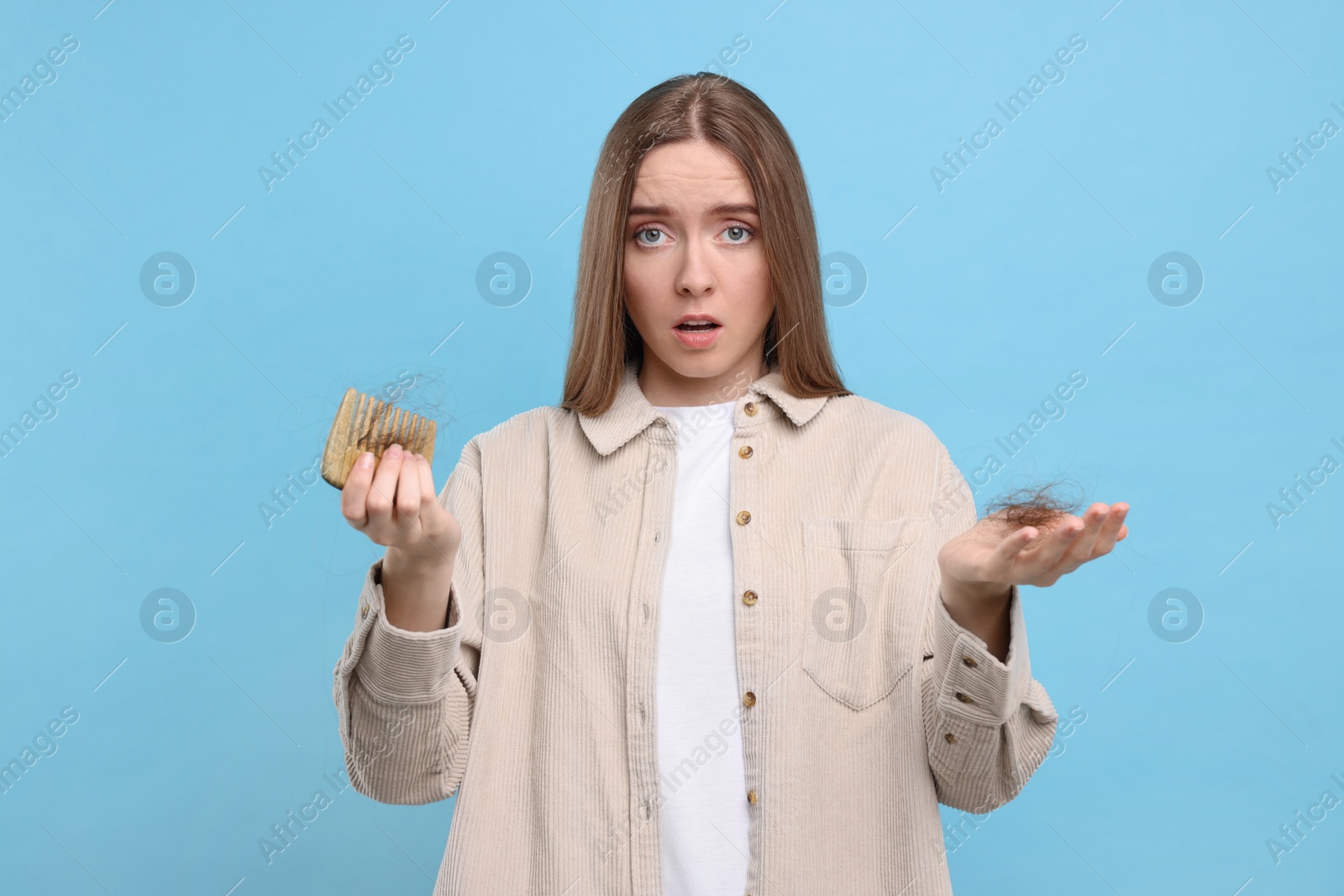 Photo of Emotional woman holding comb with lost hair on light blue background. Alopecia problem