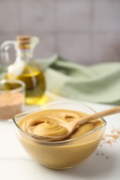 Photo of Spoon and glass bowl with tasty mustard sauce on white table