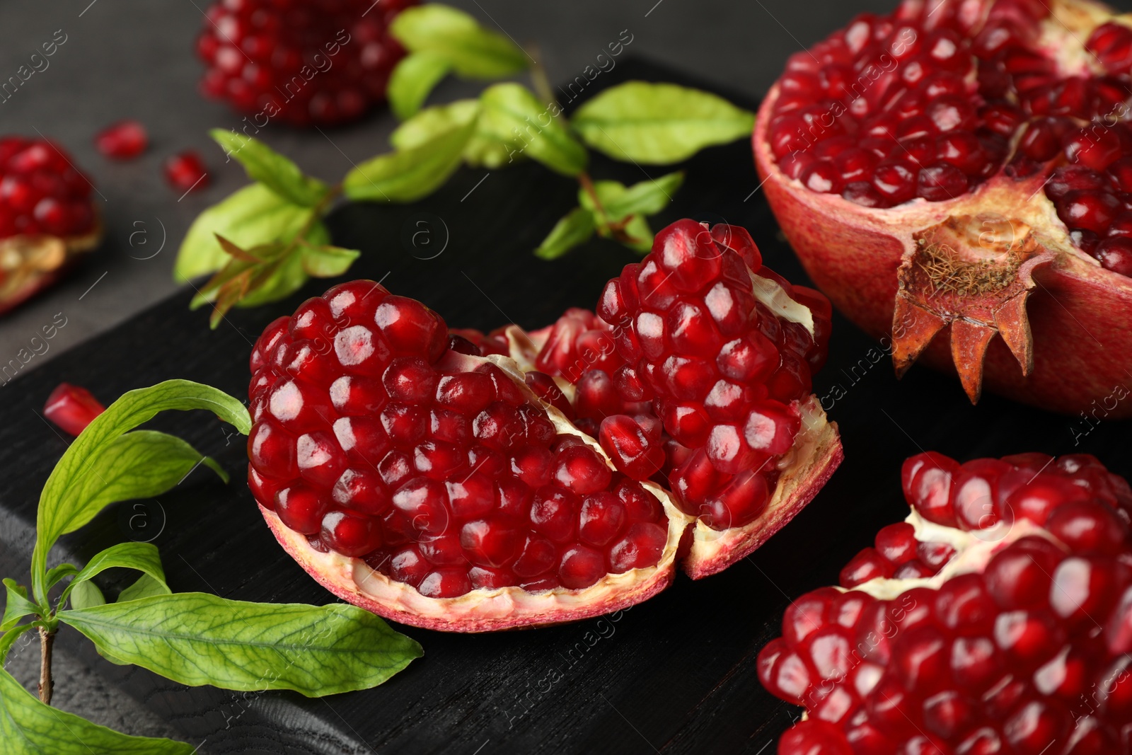 Photo of Cut fresh pomegranate and green leaves on table, closeup