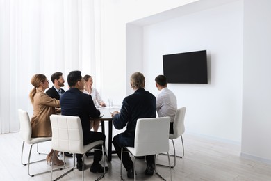 Photo of Business conference. Group of people watching presentation on tv screen in meeting room