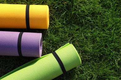 Bright exercise mats on fresh green grass outdoors, flat lay. Space for text