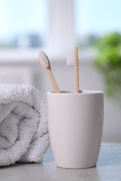 Photo of Bamboo toothbrushes in holder and towel on light grey table