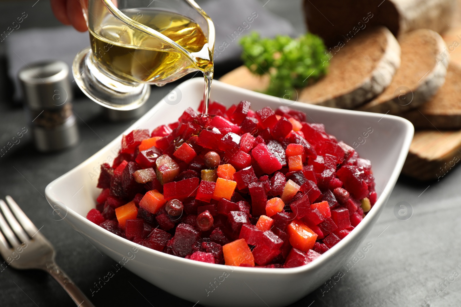 Photo of Adding oil to traditional Russian salad vinaigrette on grey table, closeup