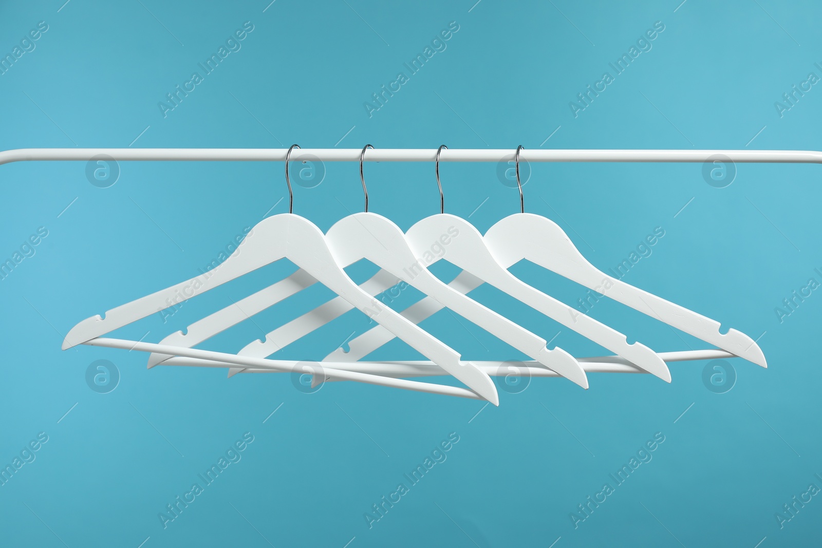 Photo of Empty clothes hangers on rack against light blue background