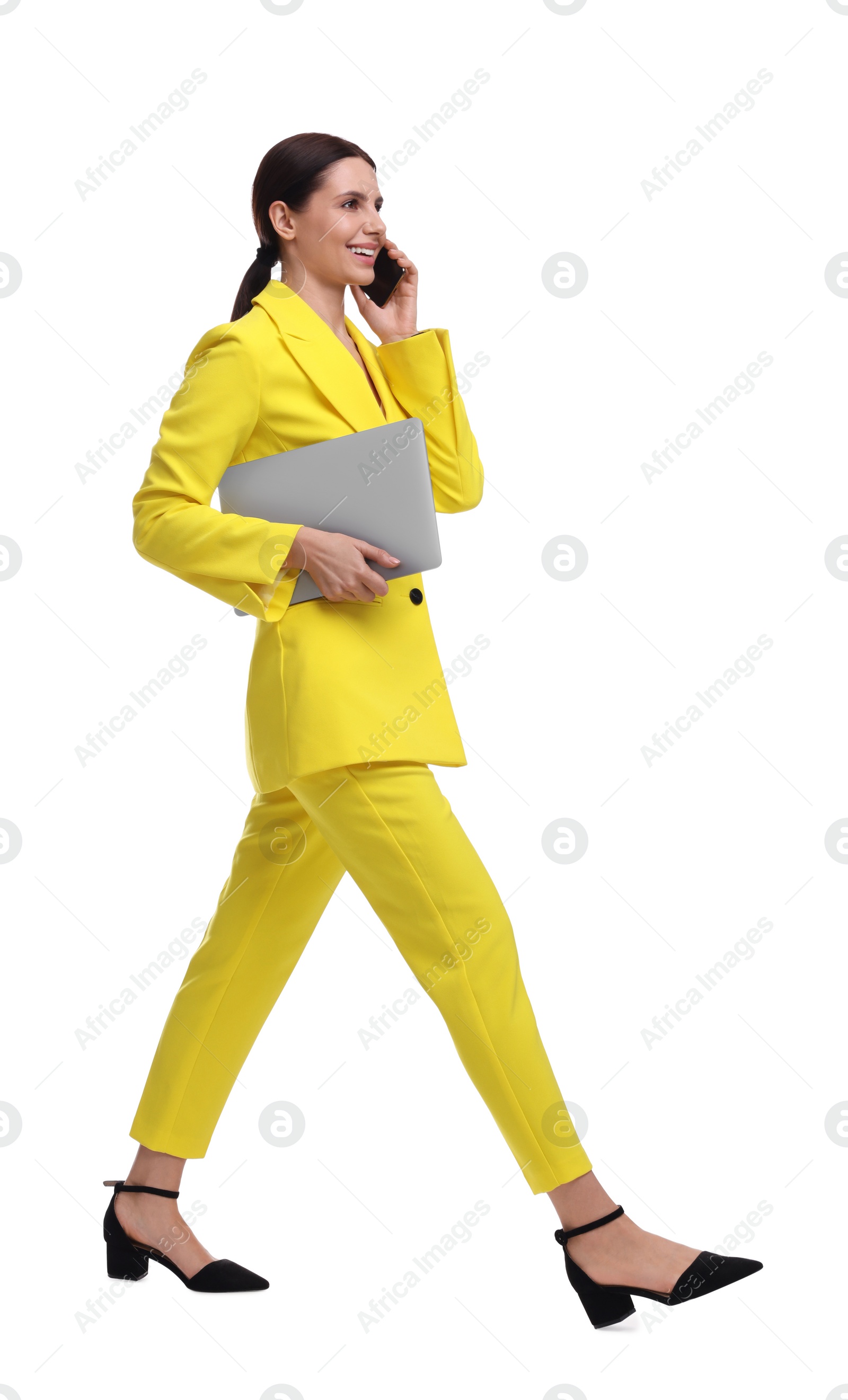 Photo of Beautiful businesswoman in yellow suit with laptop talking on smartphone against white background