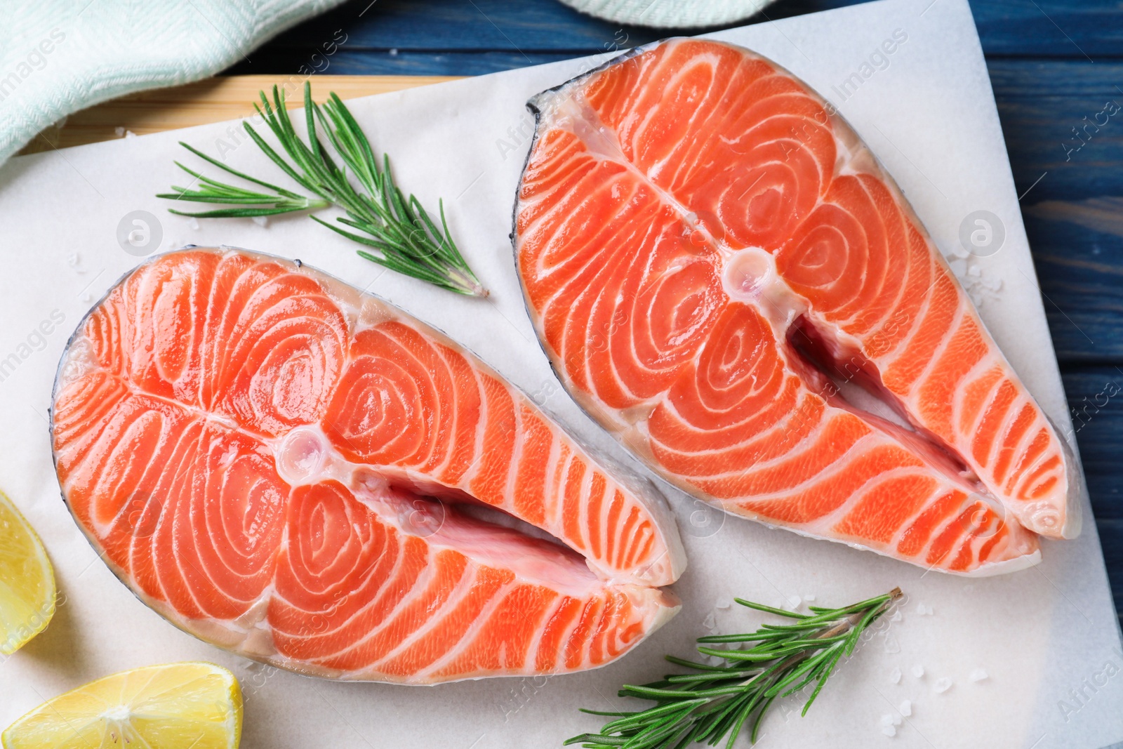 Photo of Fresh raw salmon with lemon and rosemary on parchment, flat lay. Fish delicacy