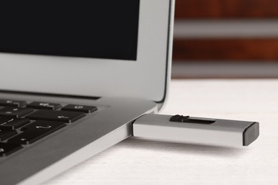 Photo of Usb flash drive attached into laptop on wooden table, closeup