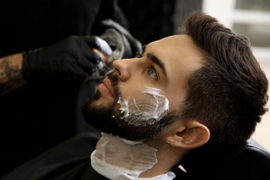 Photo of Young man with shaving foam on face in barbershop. Professional service