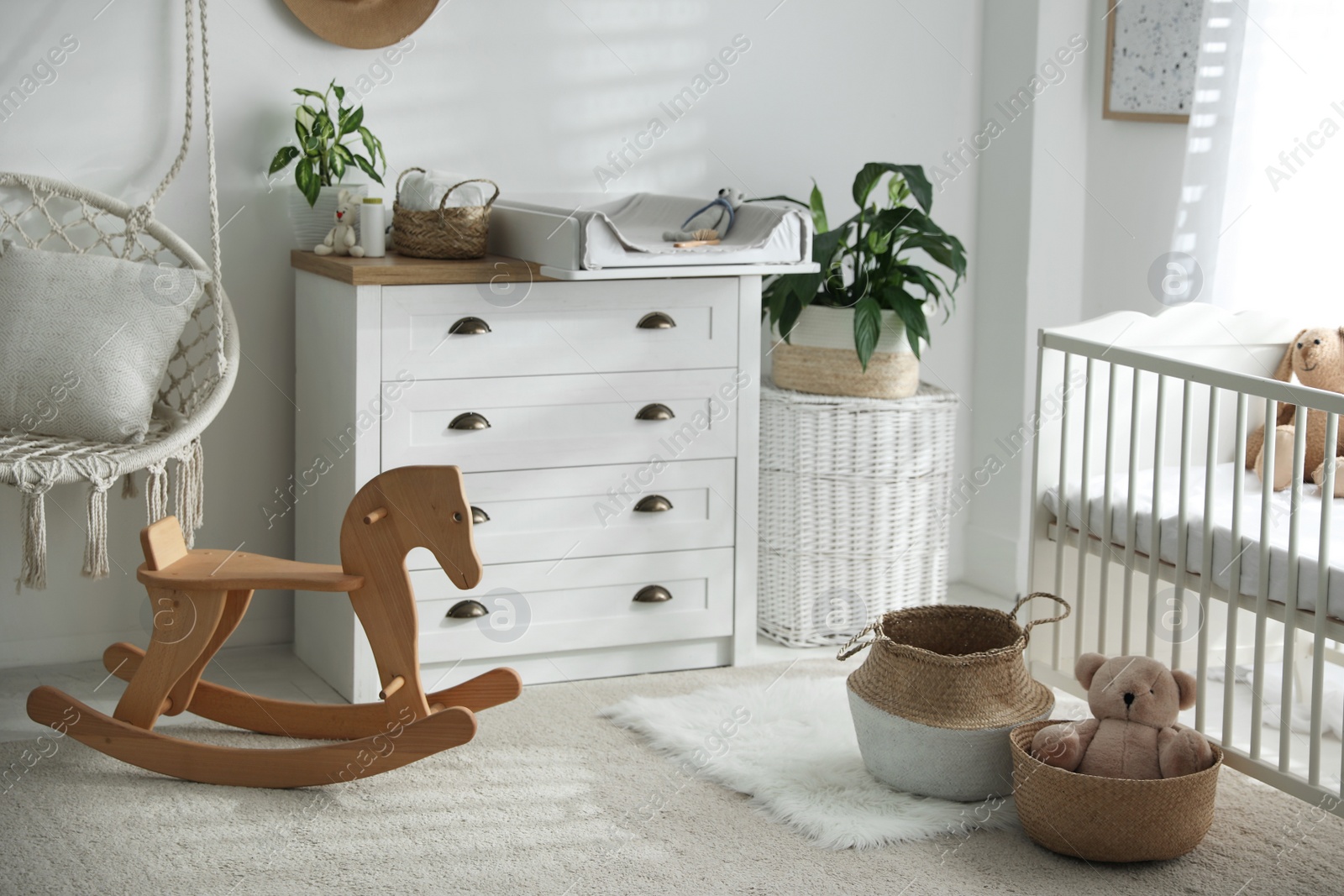 Photo of Chest of drawers with changing tray and pad near comfortable cradle in baby room. Interior design