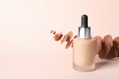 Bottle of skin foundation and decorative branch on beige background, space for text. Makeup product