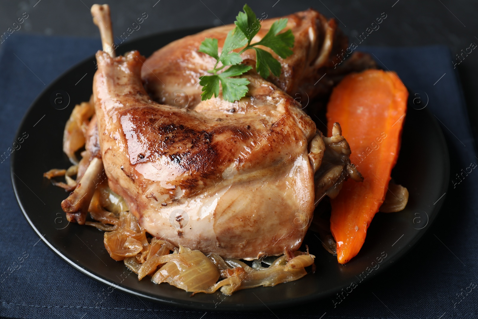 Photo of Tasty cooked rabbit meat with vegetables and parsley on table, closeup