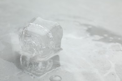 Photo of One clear ice cube on light grey table, closeup. Space for text