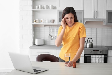 Photo of Young woman suffering from headache in kitchen