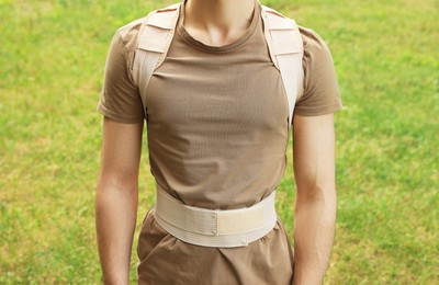 Photo of Closeup view of man with orthopedic corset on green grass outdoors