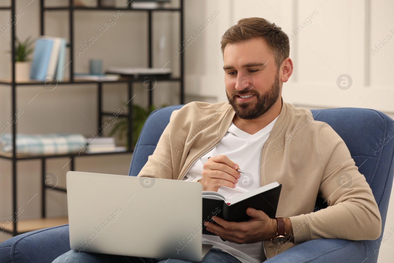 Photo of Young man working with notebook and laptop at home