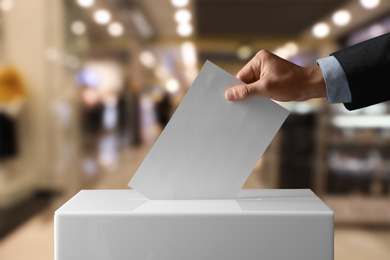 Man putting his vote into ballot box indoors, closeup