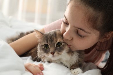 Photo of Cute little girl with cat lying on bed at home, closeup. First pet