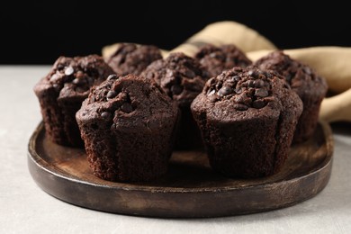 Photo of Board with delicious chocolate muffins on light table, closeup