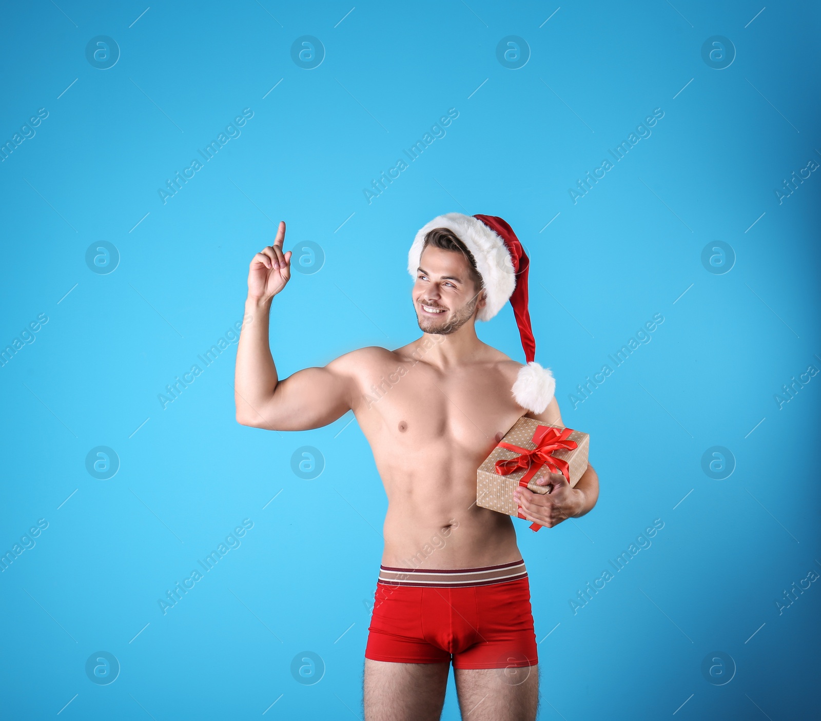 Photo of Shirtless sexy young Santa Claus with gift on color background