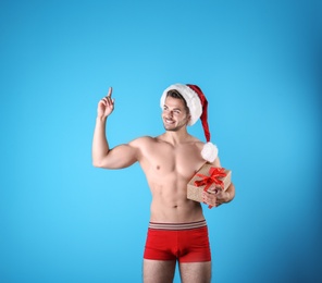 Photo of Shirtless sexy young Santa Claus with gift on color background