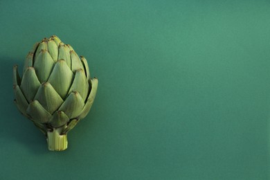 Whole fresh raw artichoke on green background, top view. Space for text